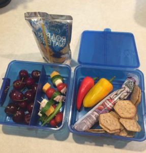 Blue lunchbox with cherries, caprese kabobs, peppers, yogurt, and whole wheat crackers. Drink is a Capri Sun.